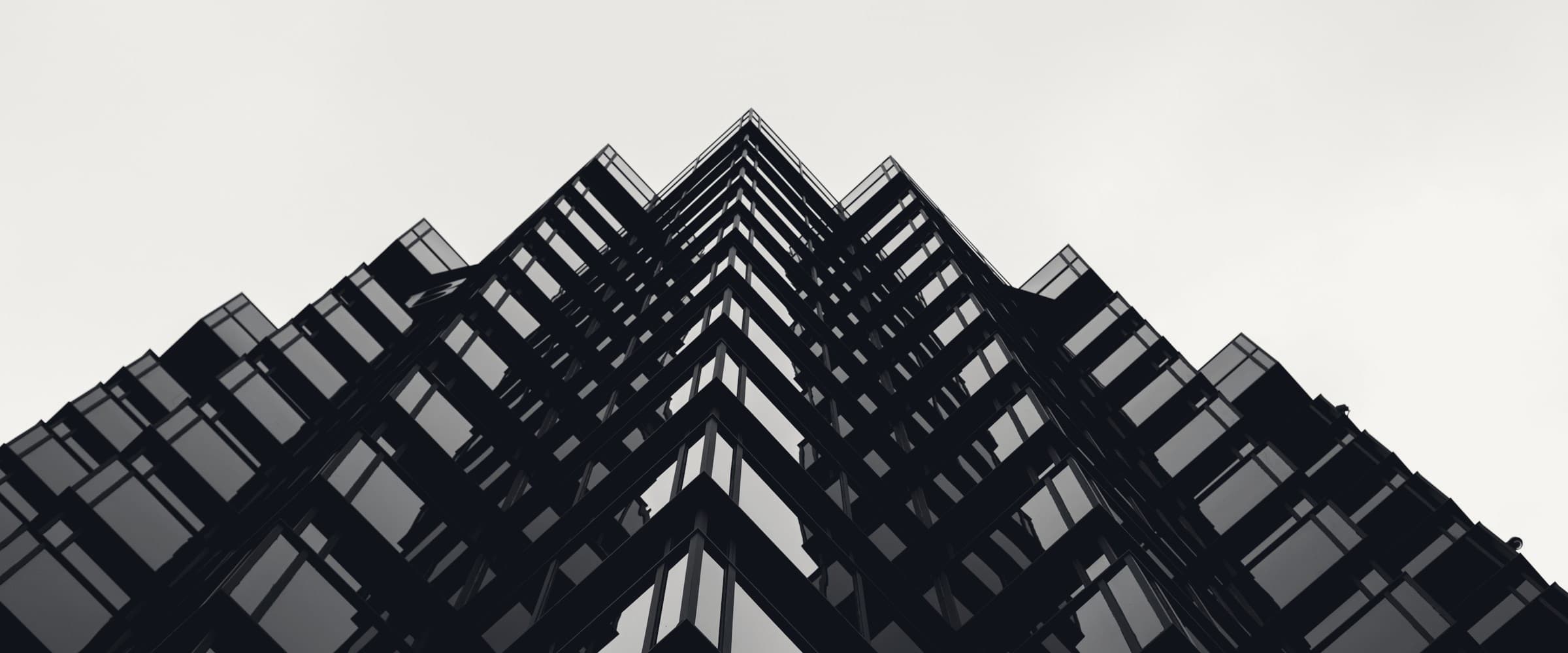 A dark angular office tower seen from below against a bright sky.