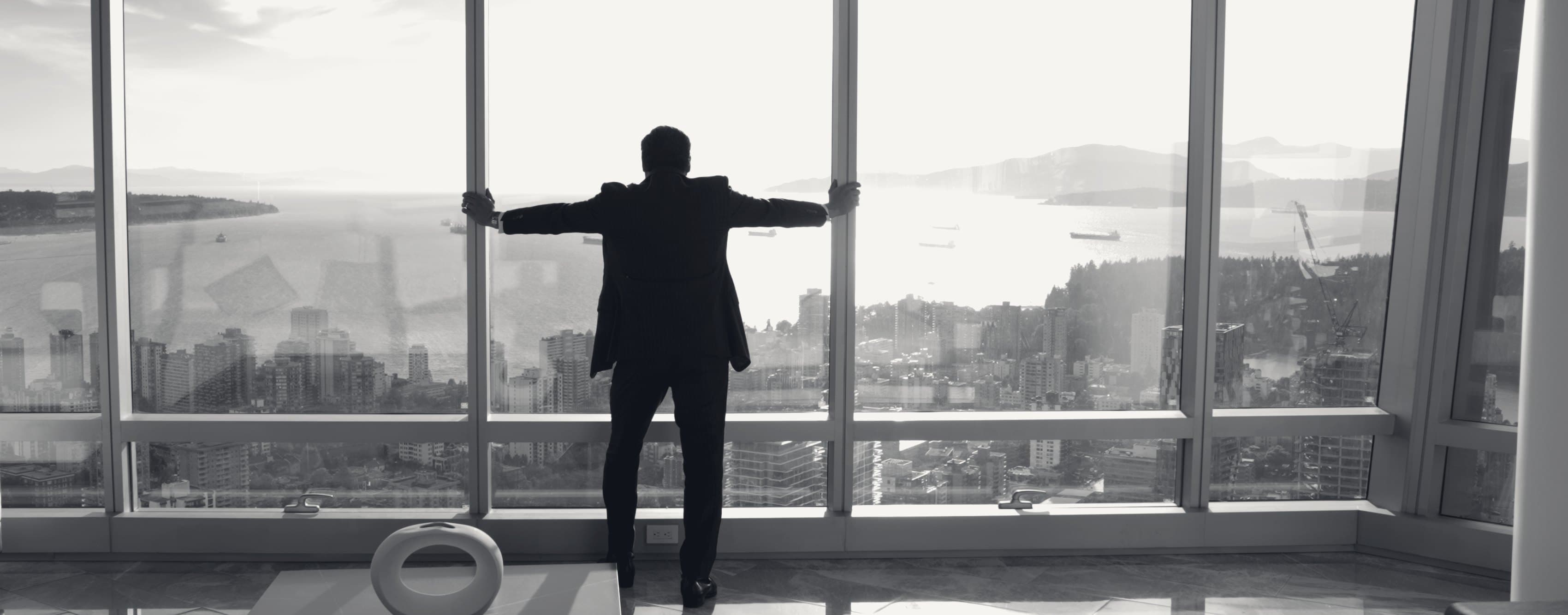 A principal at the window of a Vancouver tower, the harbour and the North Shore beyond.