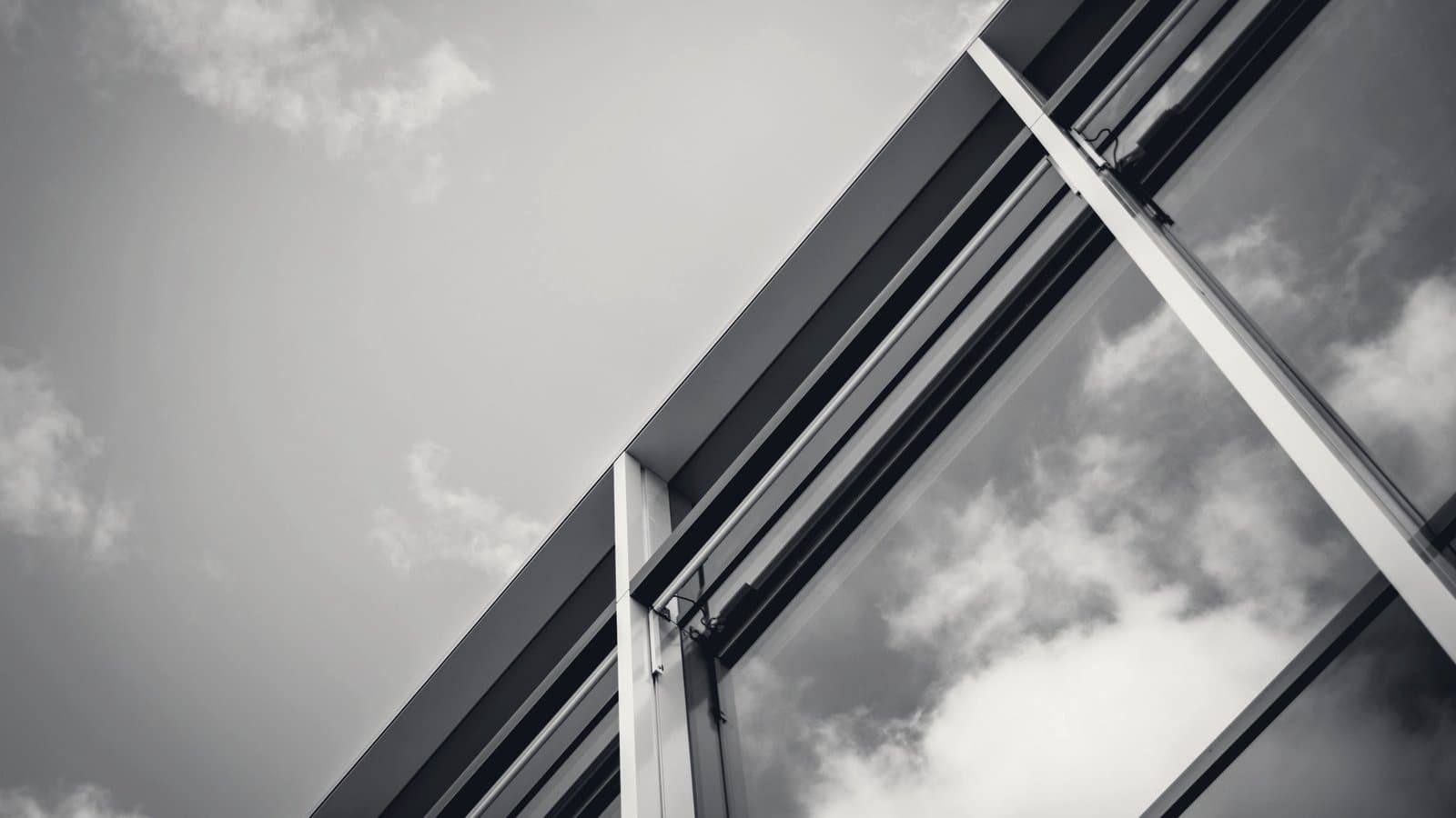 A glass curtain wall angled upward against overcast sky.