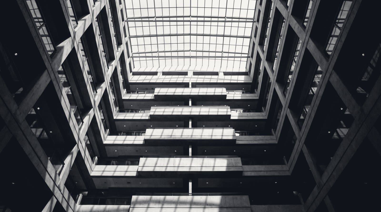 A rectilinear office atrium seen from the floor, identical balcony levels stacked to a glazed roof.