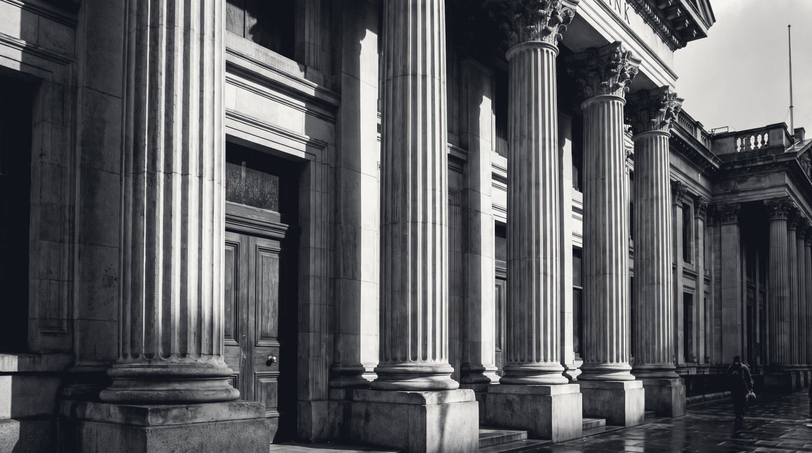 The deep stone portico of a classical bank building, heavy columns in raking light.