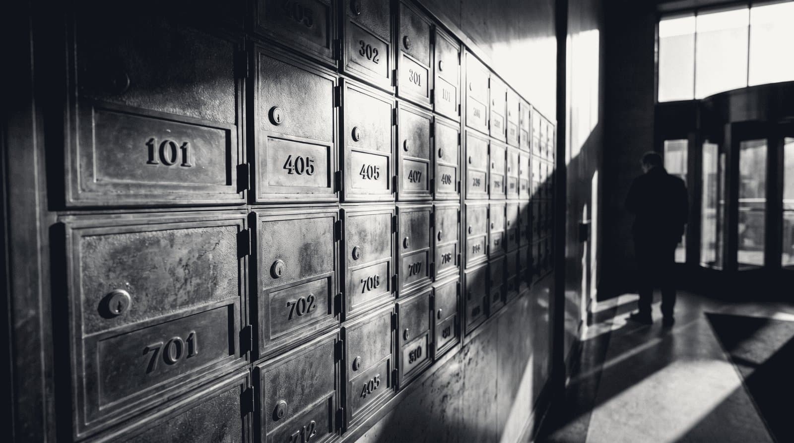 A wall of small brass mailboxes with engraved number plates in an office building vestibule.