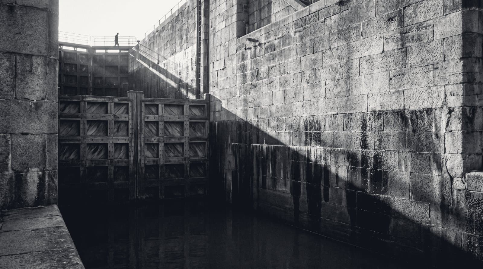 A canal lock chamber with its heavy gates closed, deep water marks staining the stone walls.
