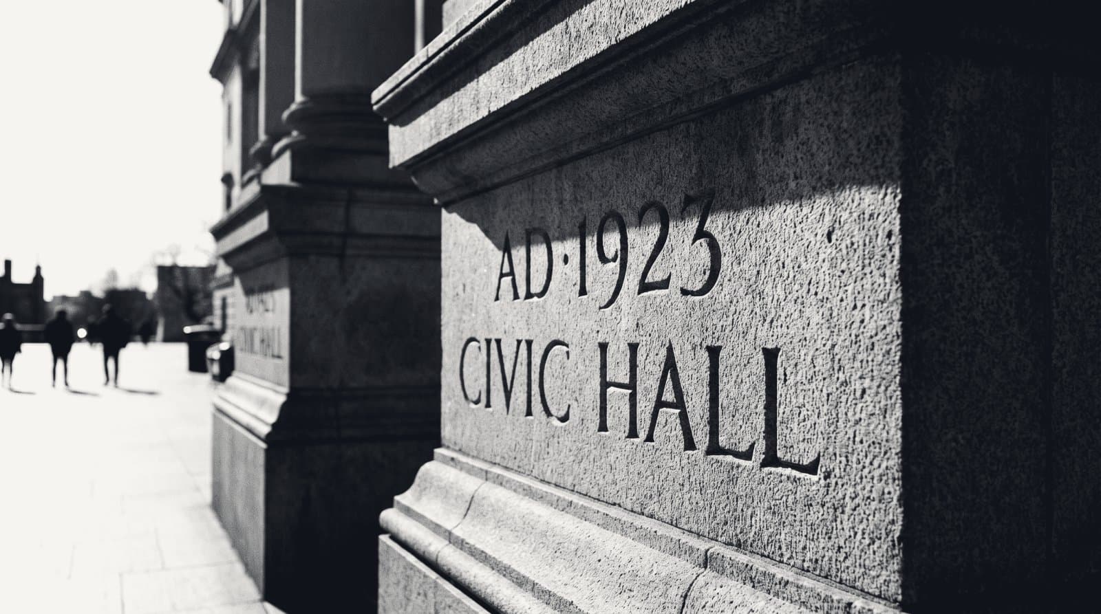 The carved cornerstone of a stone civic building, incised date lettering in raking light.