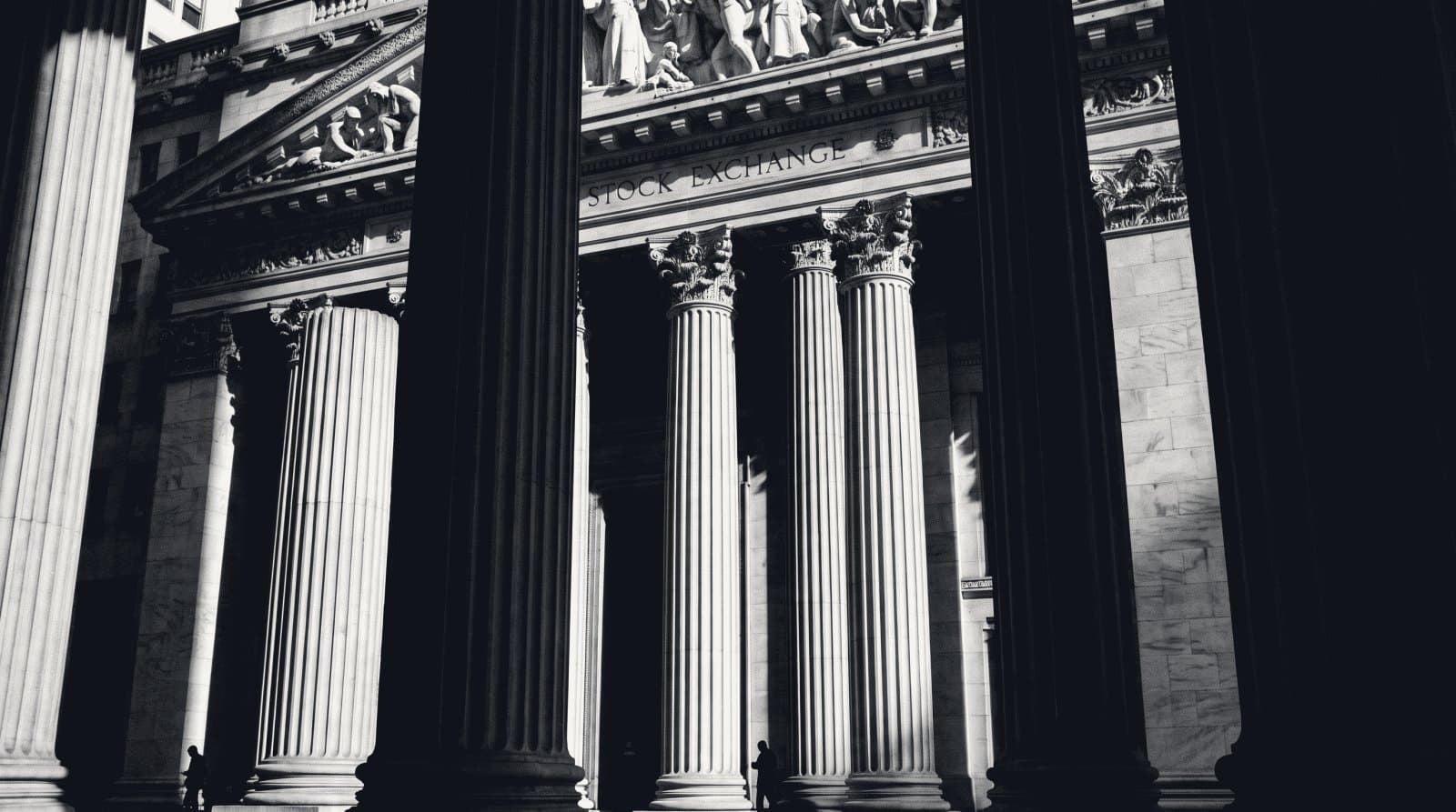 The fluted stone columns and pediment of a neoclassical exchange portico, seen from below in hard side light.