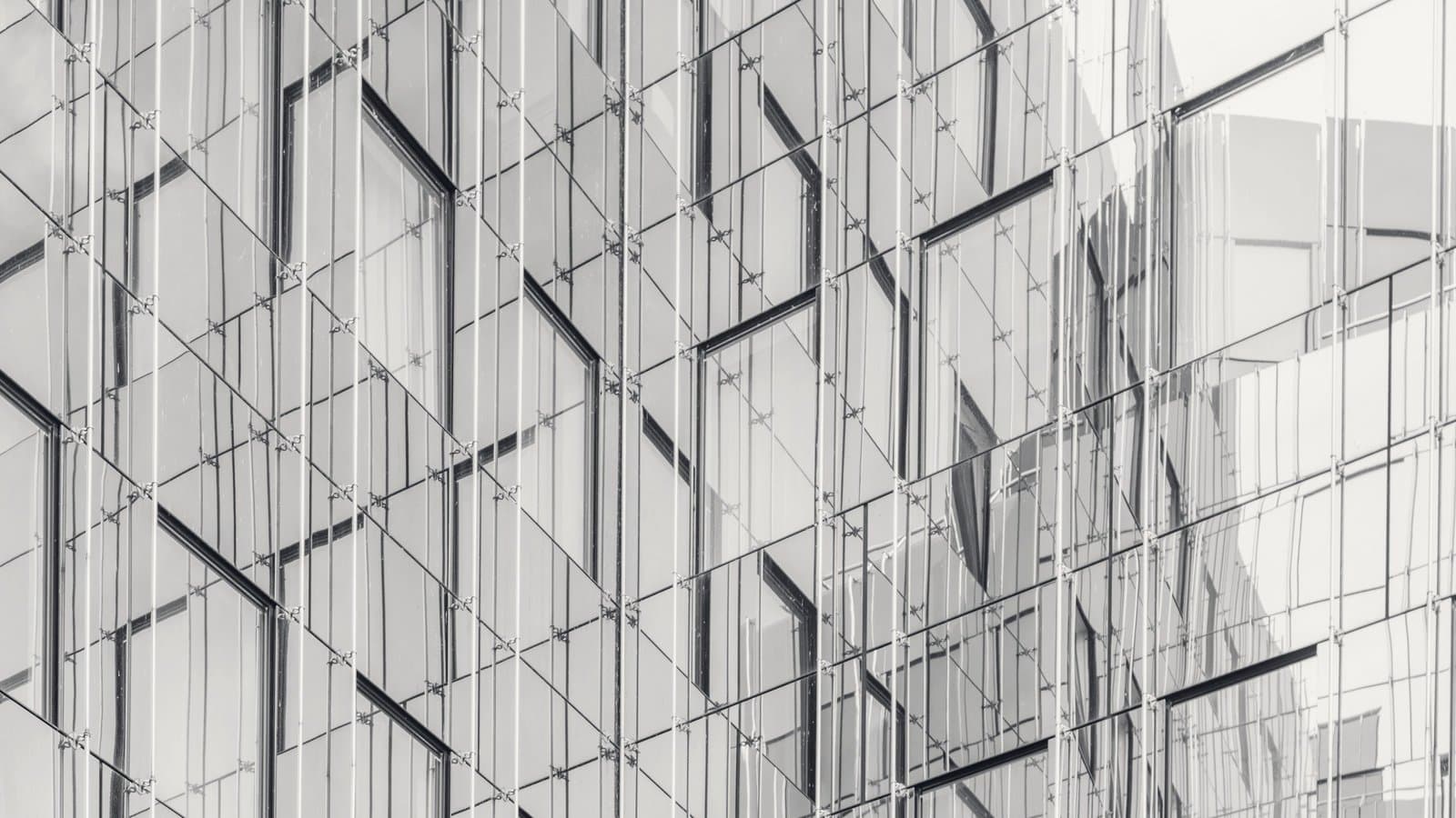 A faceted glass curtain wall, each panel reflecting a slightly different version of the building opposite.
