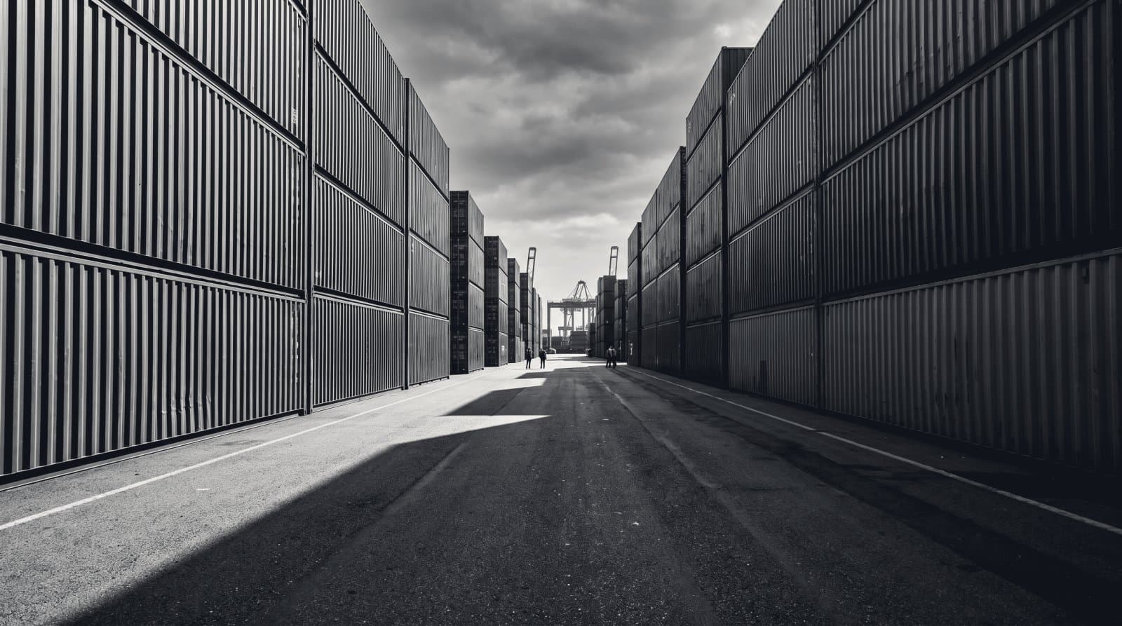 Shipping containers stacked five high in a port yard, a canyon of corrugated steel running away from the camera.