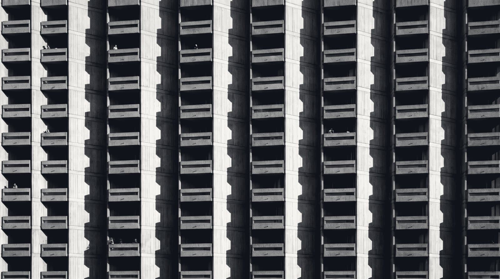 A repeating grid of concrete residential balconies on a housing block, seen straight on in raking light.