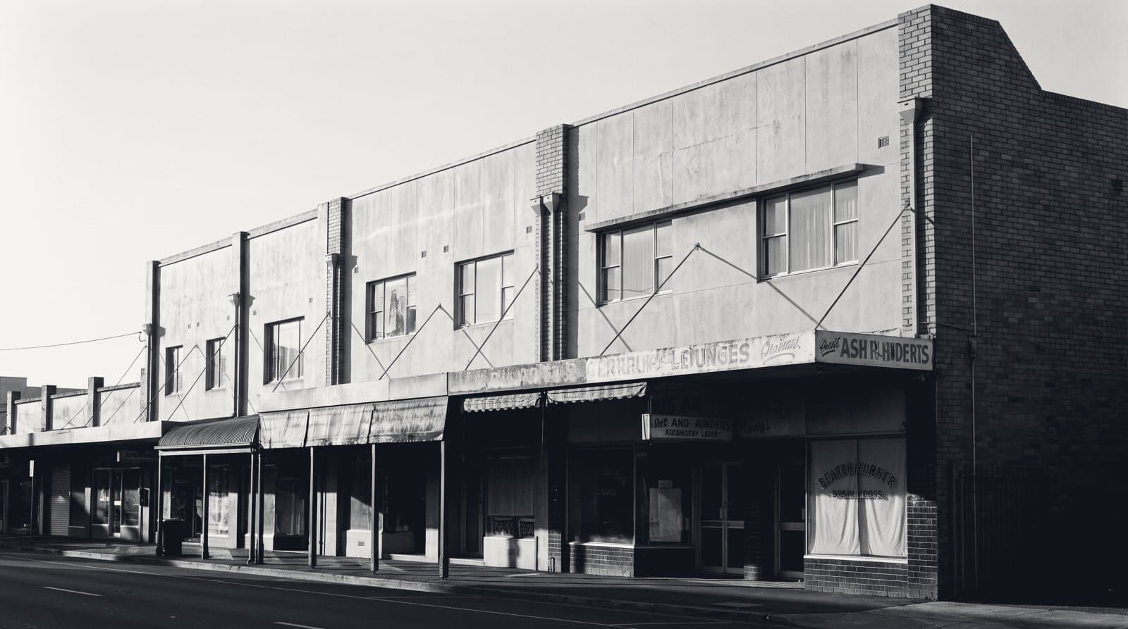A row of small two-storey commercial buildings on an empty street in strong late sidelight.