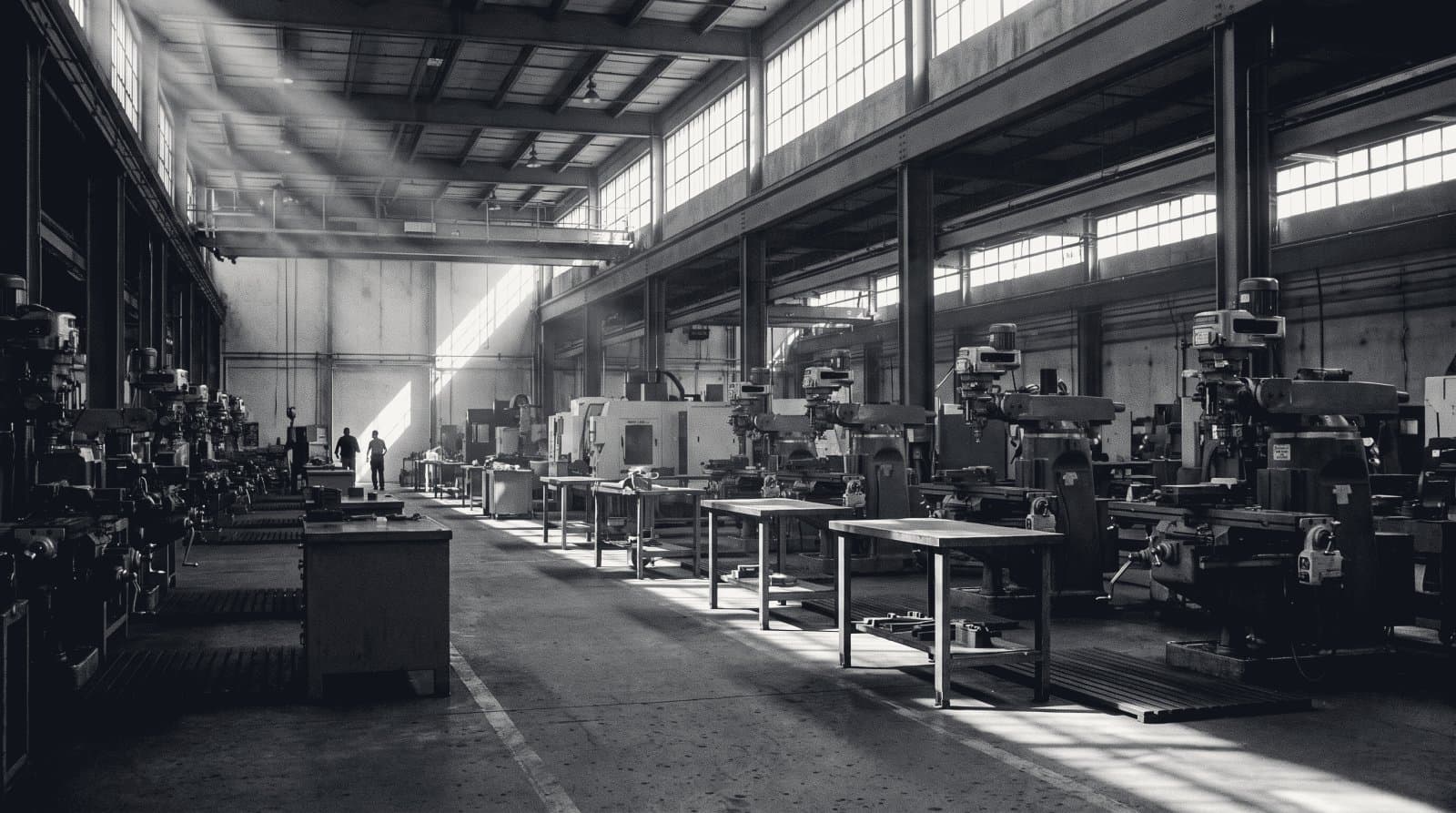 The interior of a precision machine shop with rows of milling machines under high clerestory windows.
