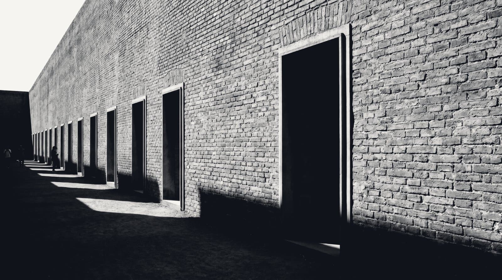 A long brick wall pierced by a row of identical open doorways receding into distance.