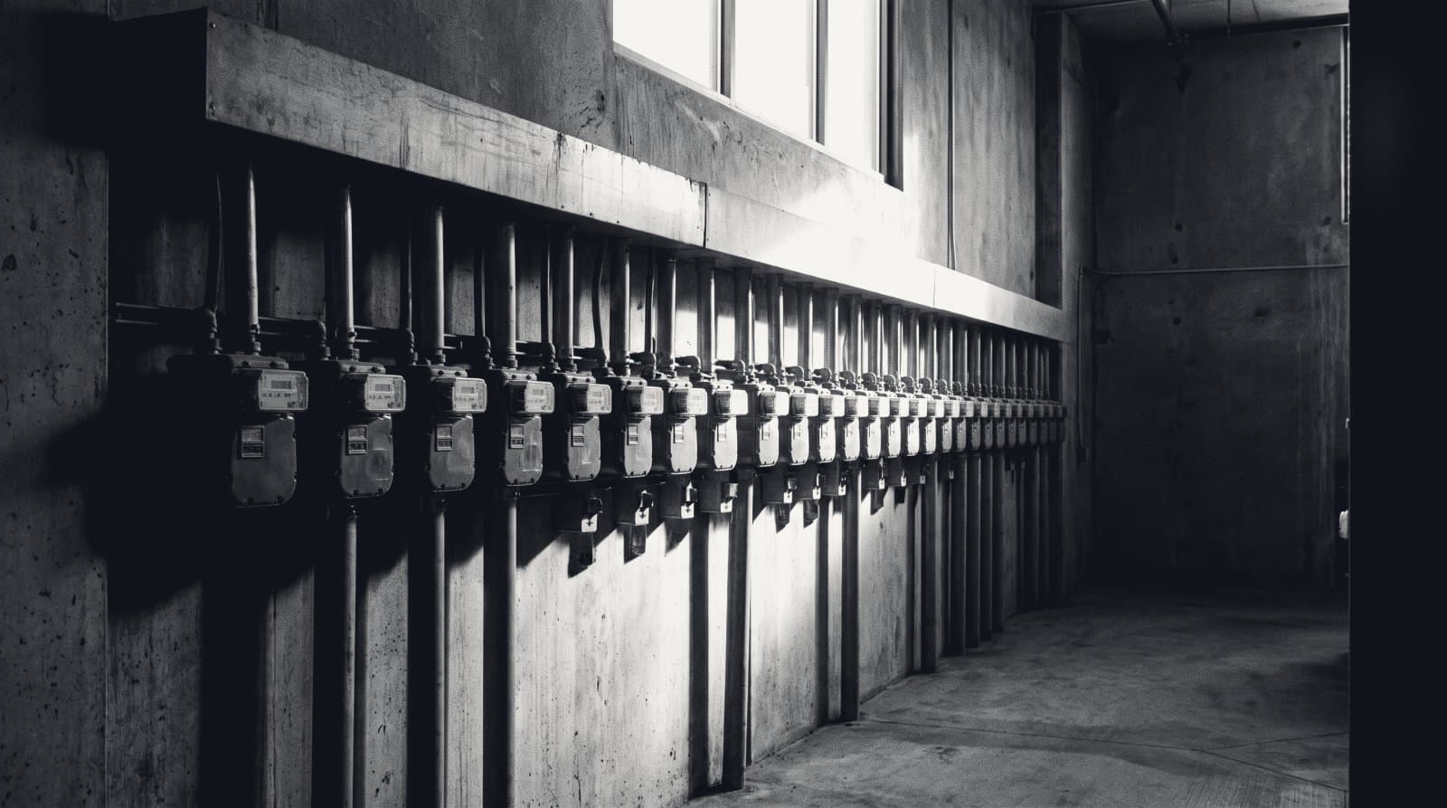 A wall-mounted row of identical utility meters and conduit in a service corridor.