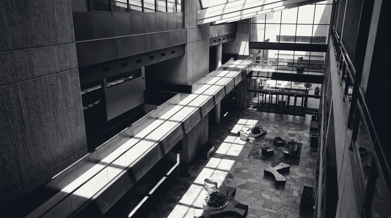 A mezzanine balustrade above a corporate atrium, one long diagonal shadow across the void.