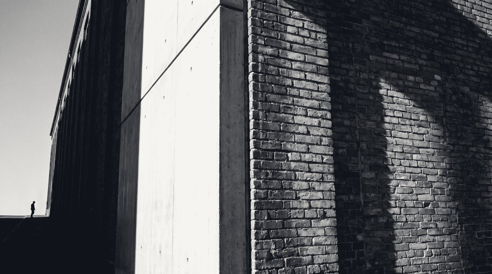 The vertical seam where new smooth concrete meets old weathered brick on a building flank.