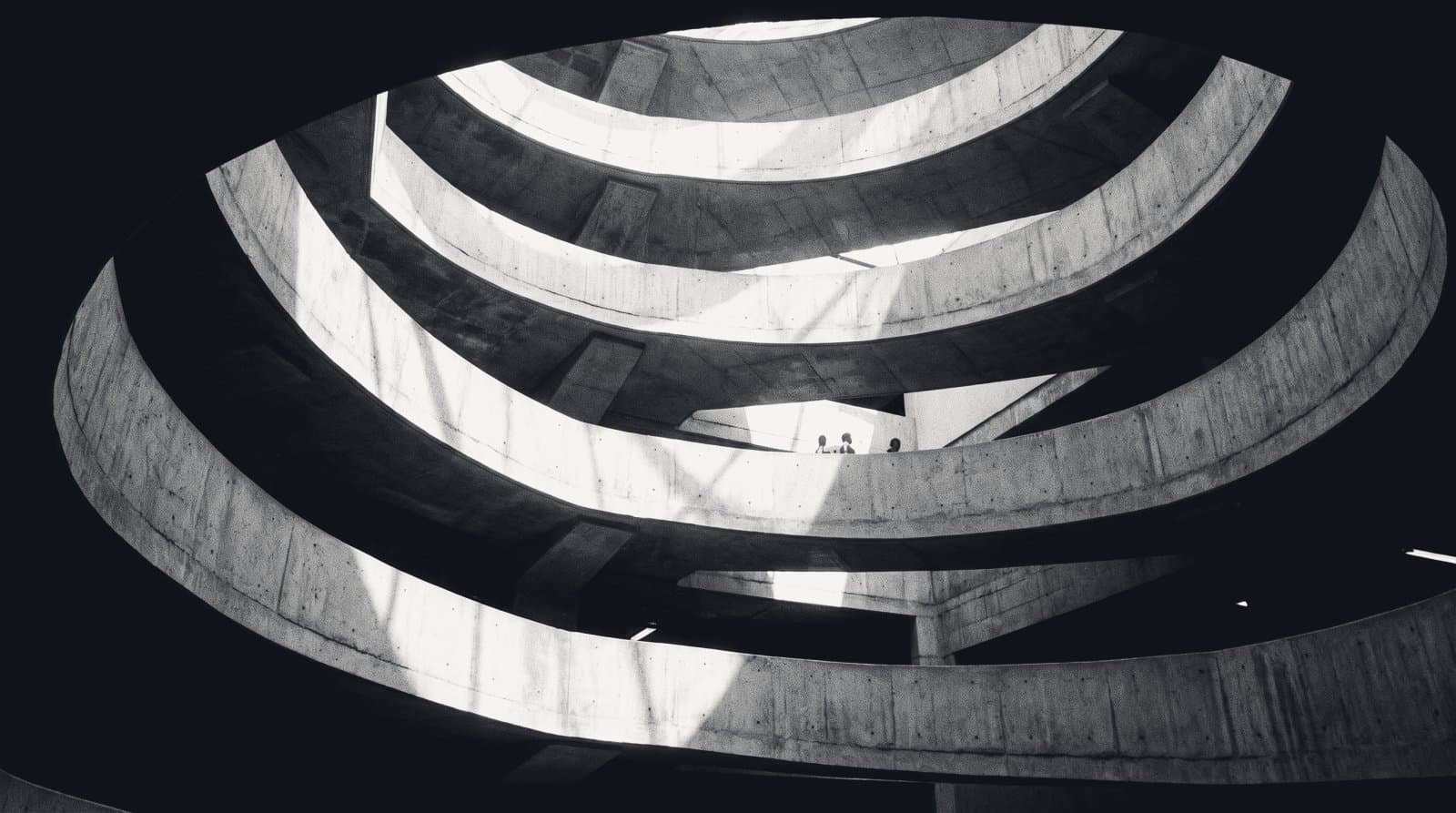 The curving concrete ramp helix of a multi-storey car park, seen from the centre looking upward.