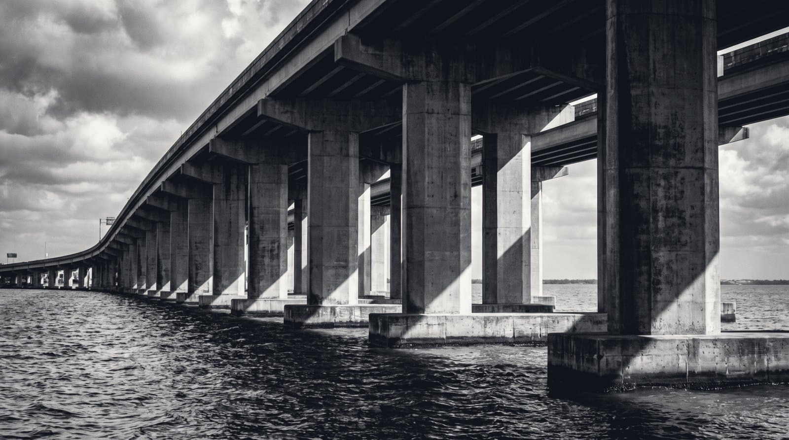 A row of concrete pier columns carrying an elevated roadway over water, receding in perspective.