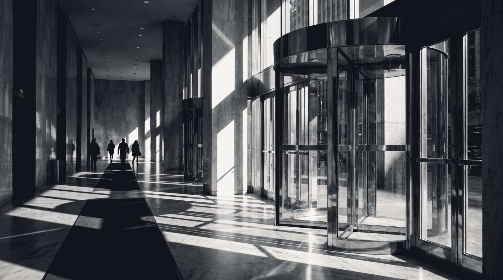 The polished brass revolving door of a corporate headquarters lobby, seen from inside against bright street light.