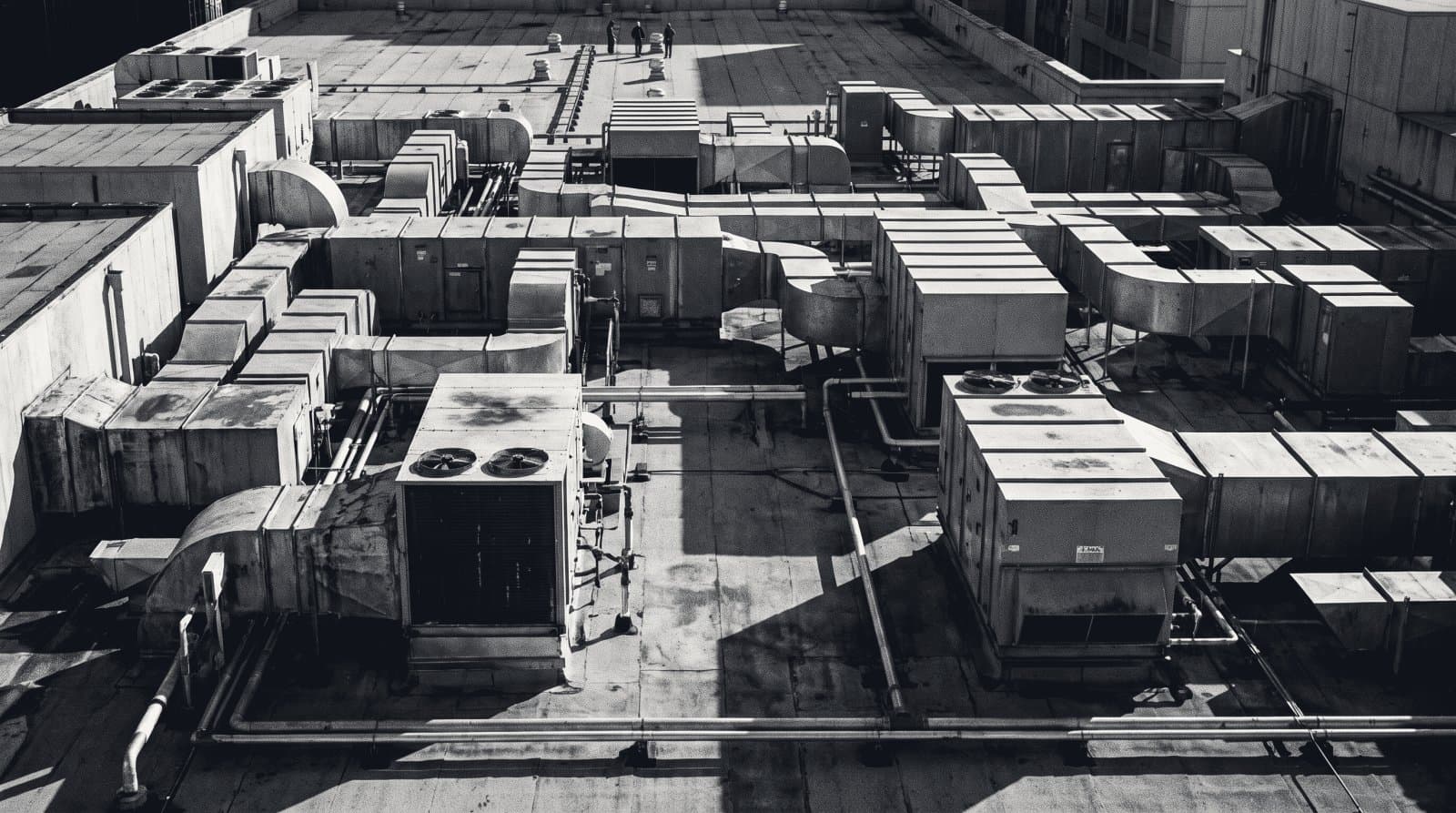 Rows of rooftop mechanical air handling units and ductwork on a flat commercial roof.