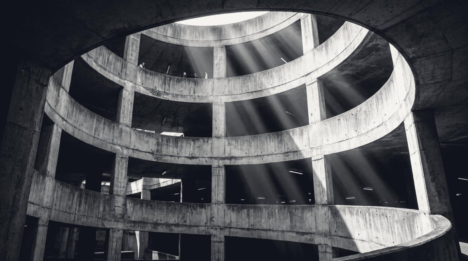 The helical vehicle ramp of a concrete car park photographed from below, coils turning upward.