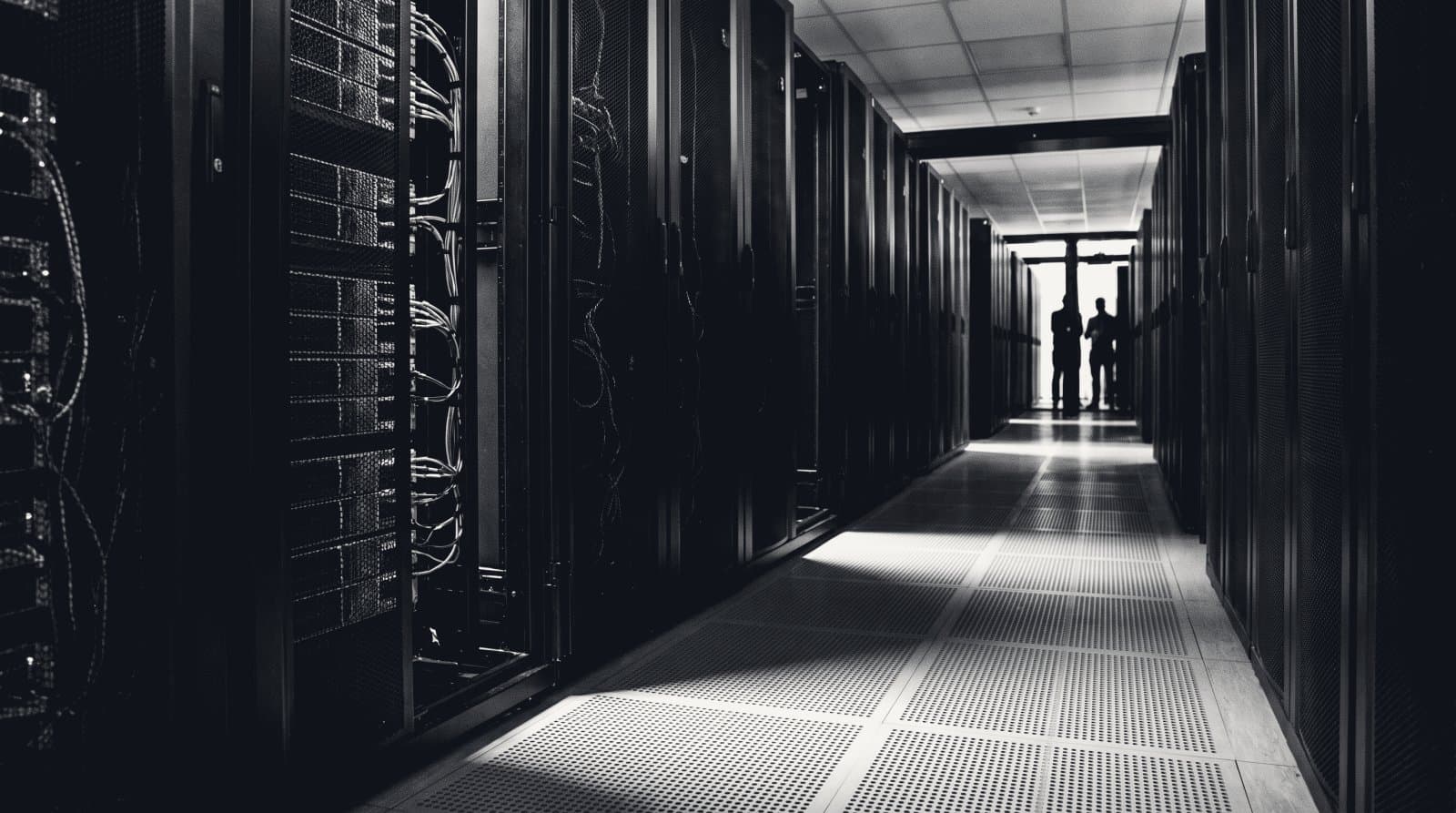 A cold aisle between two rows of tall dark server cabinets in a data centre, floor grilles receding.