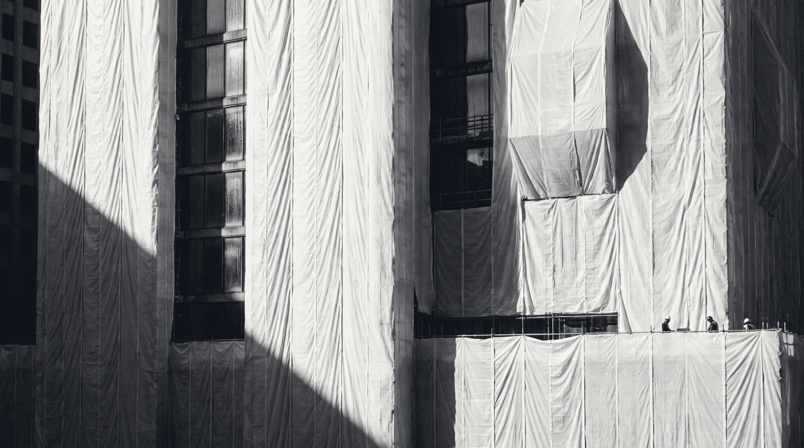 A large building facade entirely wrapped in construction sheeting, the shape showing through.