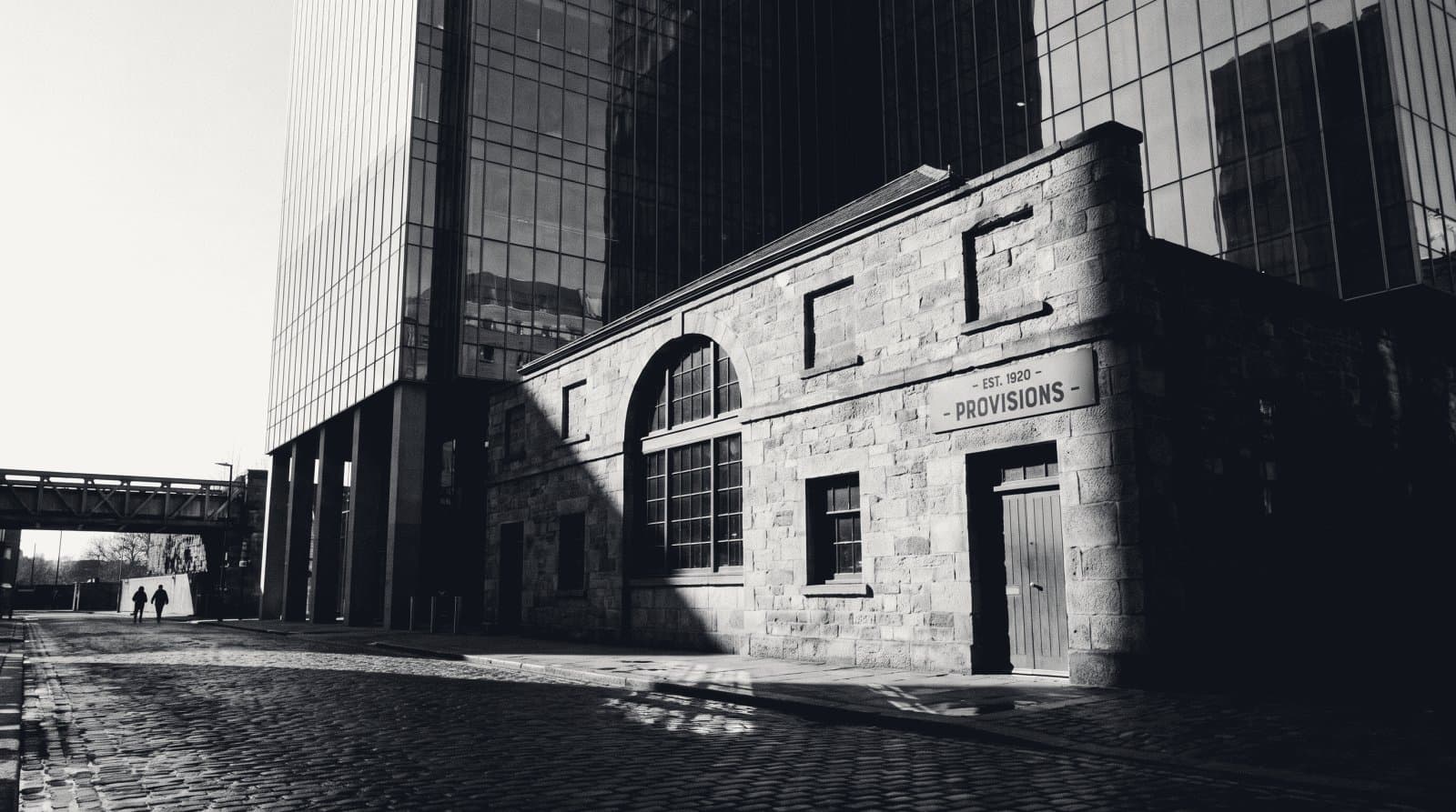 A small single-storey stone shopfront standing alone at the foot of a tall glass office tower.
