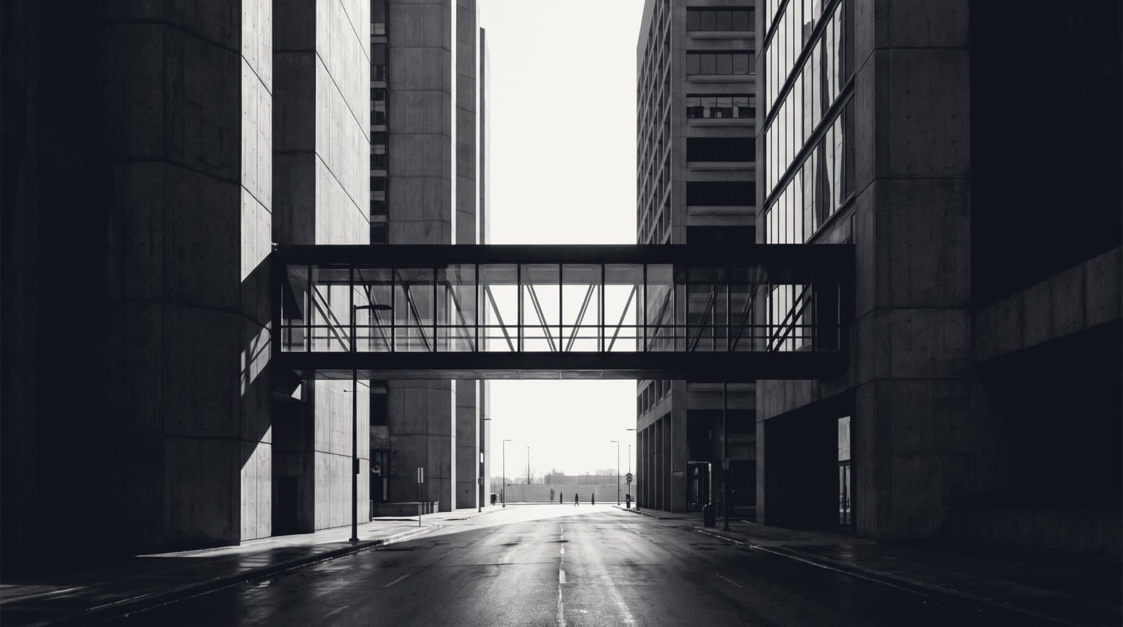 A narrow enclosed skybridge joining two tall buildings above an empty street.