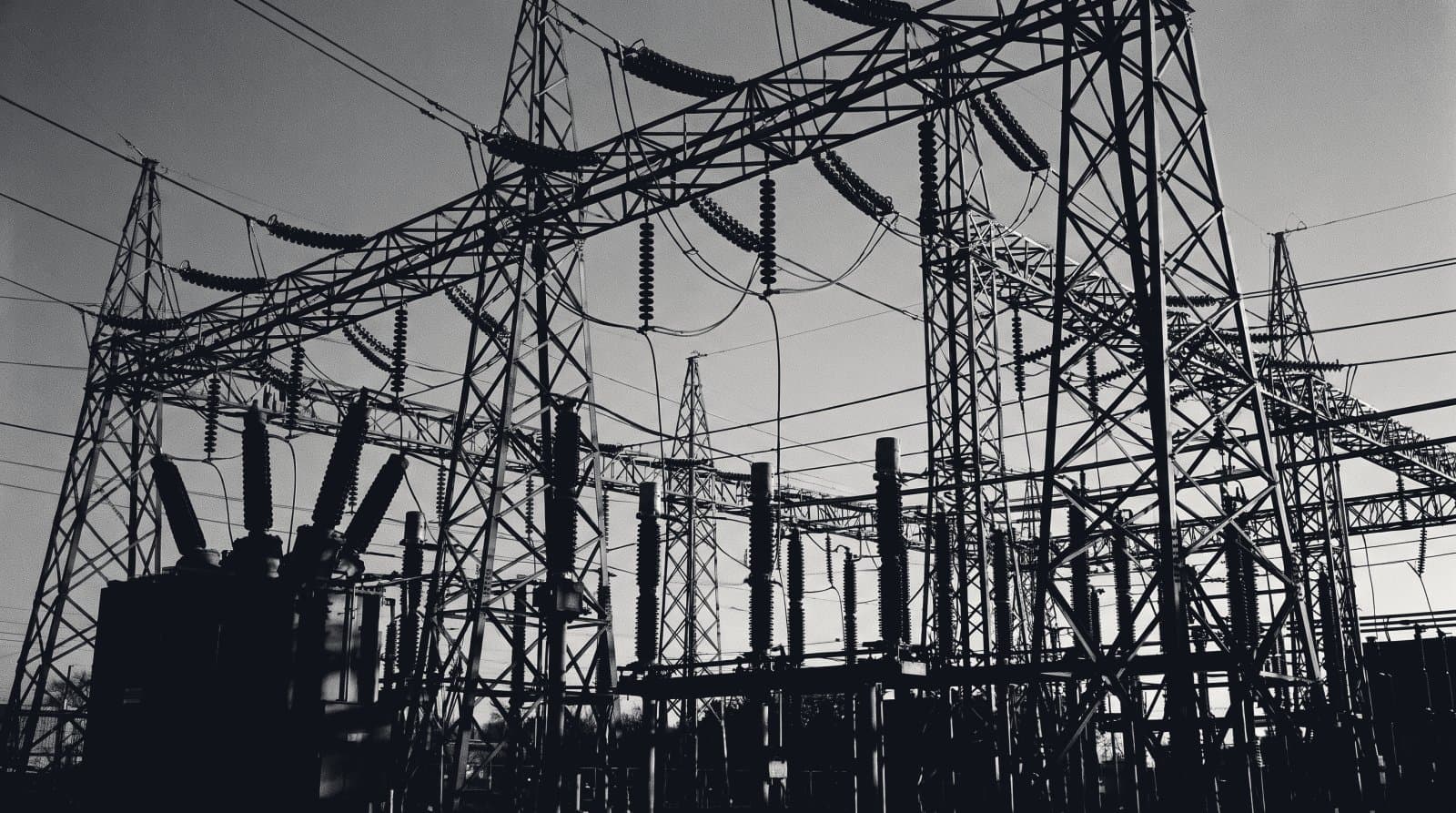 The lattice steelwork and insulator strings of an electrical substation switchyard against a dark sky.