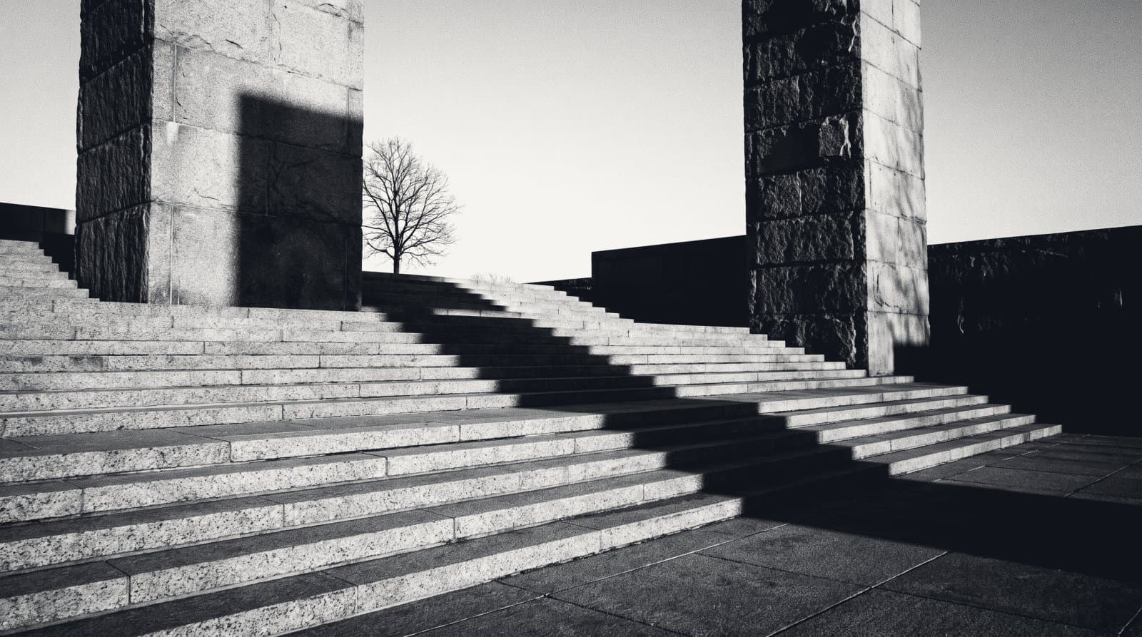 A terraced plaza of wide shallow steps descending between two towers, long shadows on every tread.
