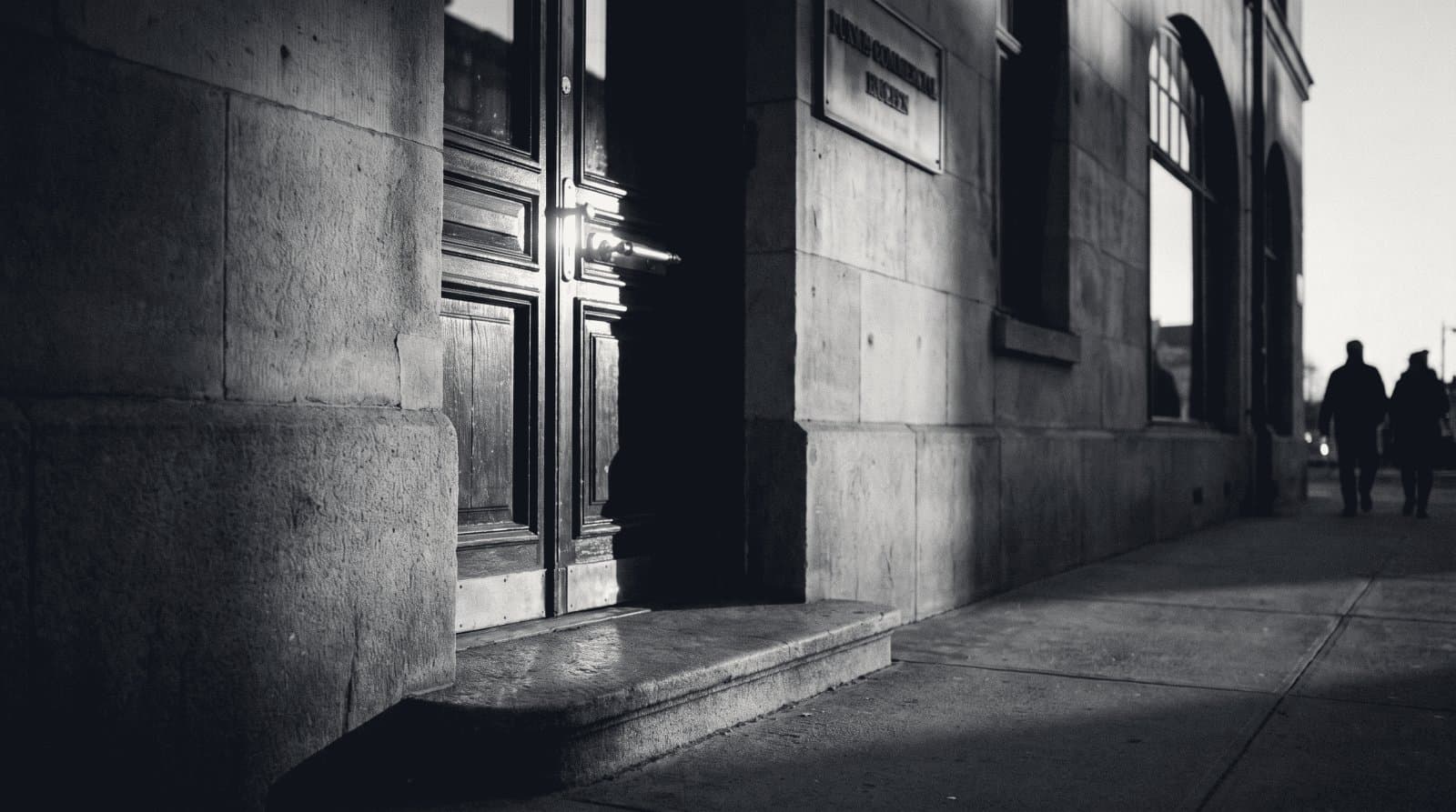 A worn stone doorstep and closed panelled door of an old commercial building, brass handle catching the light.