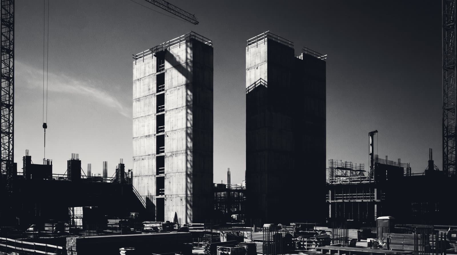 Two identical concrete service cores rising side by side, one in full light and one in deep shadow.