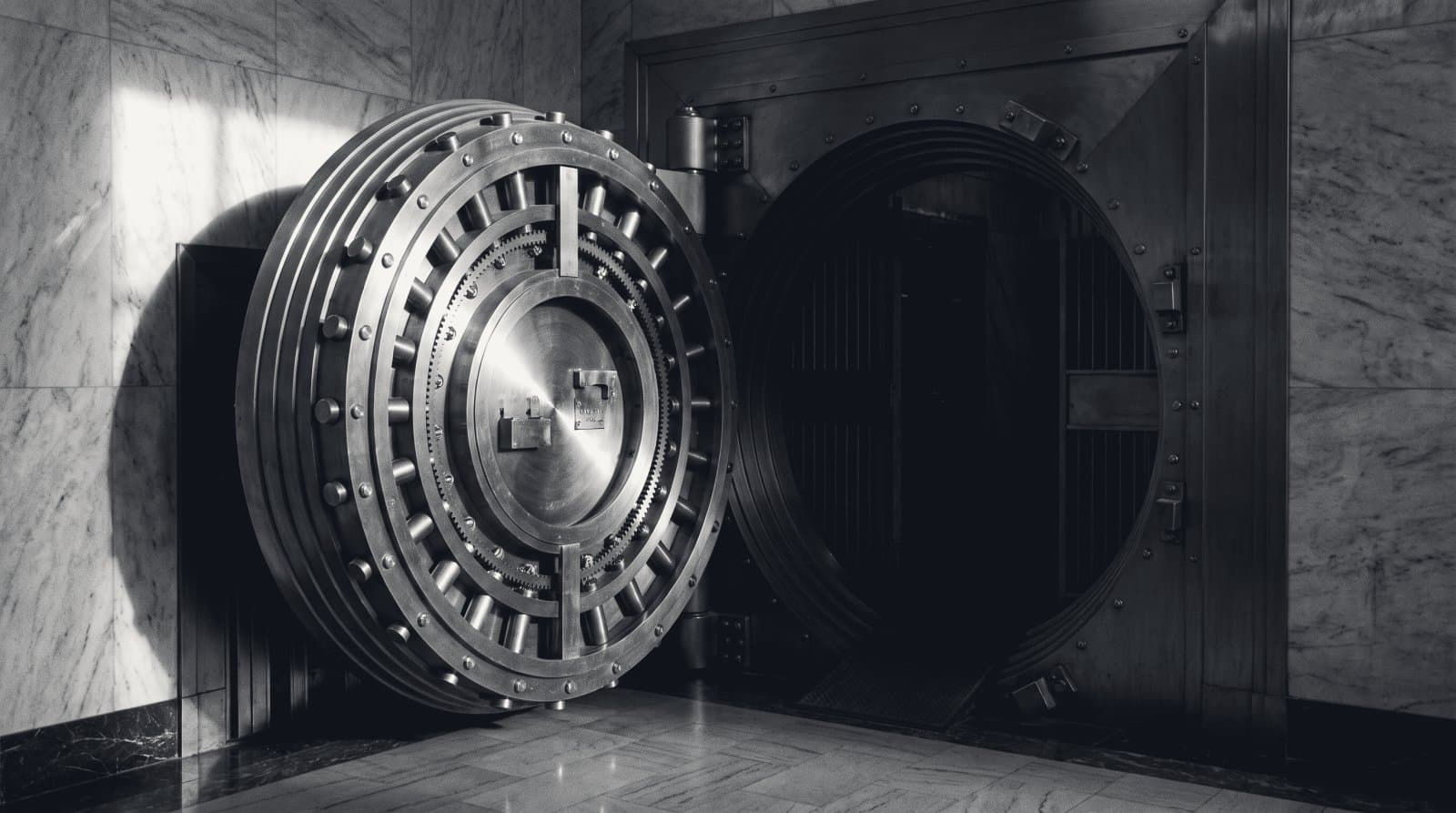 The open circular steel door of a bank vault, machined rings under one hard light.