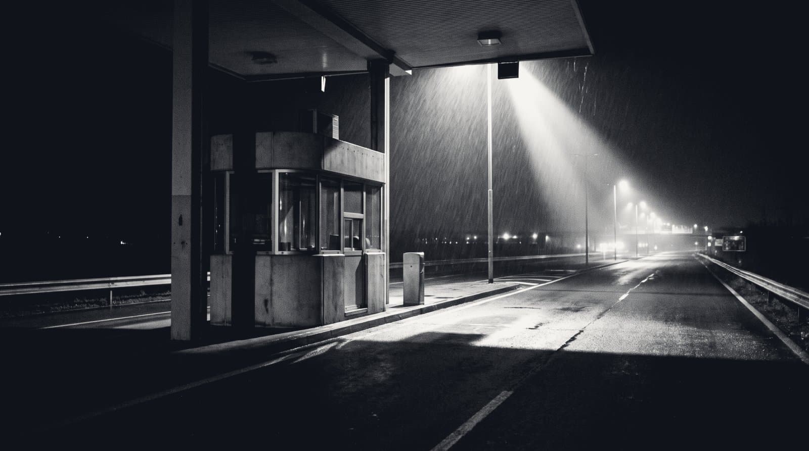 A single unattended toll booth on an empty multi-lane road at night.