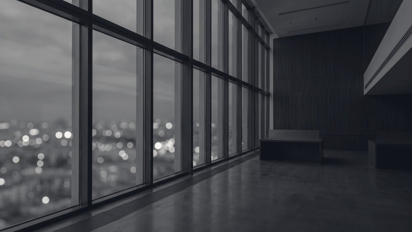 An empty high-floor office at dusk, city lights thrown out of focus beyond the glass.